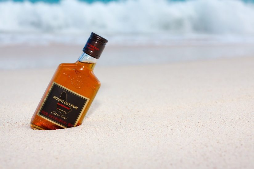 Bottle of mount gay rum stuck in the sand next to a rum shack in barbados