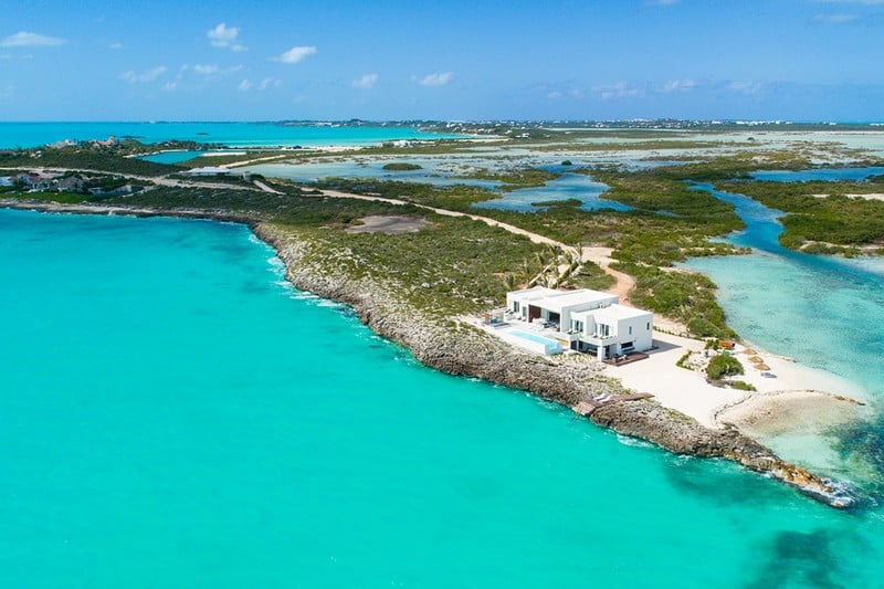 Tip of the Tail, one of our luxury Turks and Caicos Villas, sits at the end of a sandy peninsula. The view is from the air and the landscape, a lush green and blue, reaches into the distance.