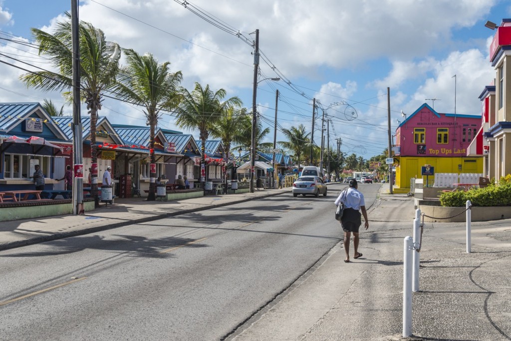 Oistins Fishing Village. A woman walks through Oistins Fishing Village with colorful shops lining either side of the street