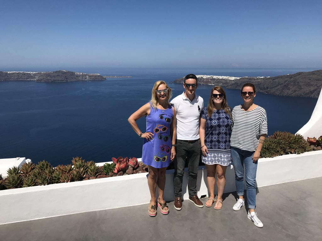 Alexandra, Linda, Sean, and a villa manager pose for a photo in front of the astonishingly pretty view from Erossea Villa