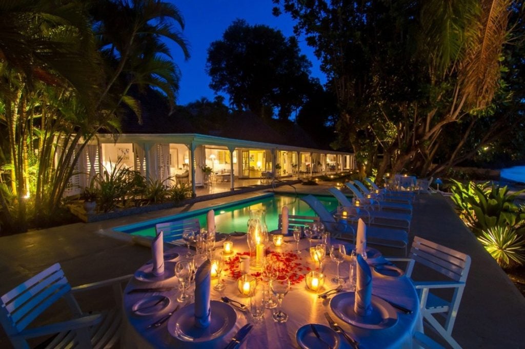 The pool area glows seductively in the Jamaican night. A prettily set dinner table scattered with rose petals and candles warms the images foreground.
