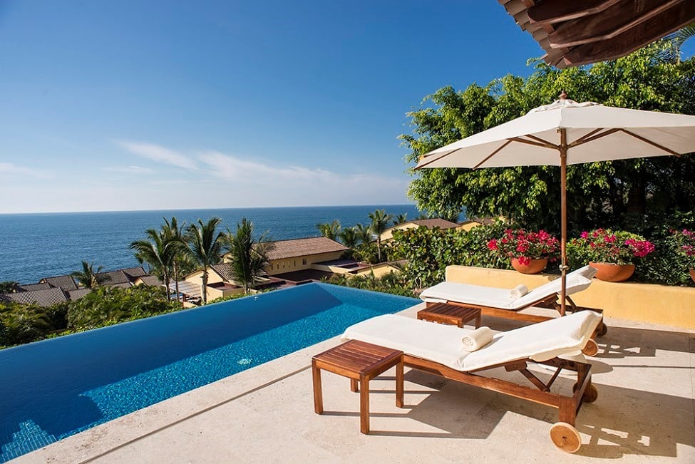 Warm tropical sun beats down on sun-loungers by a pool that glitters with deep ultramarine waters