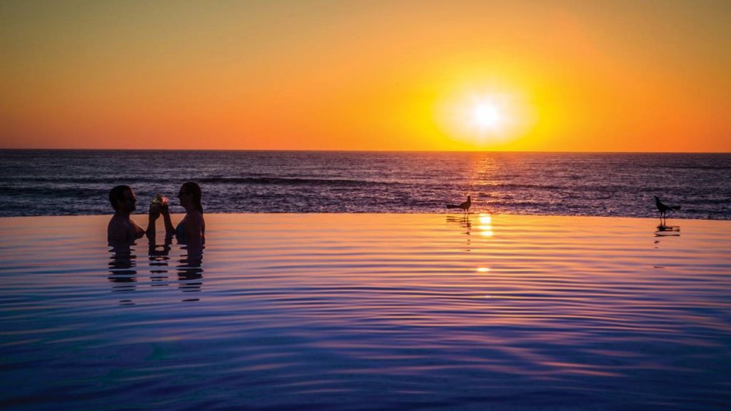 A couple share a sunset drink in a pool at Punta Mita A couple in an infinity pool silhouetted against the setting sun at Punta Mita