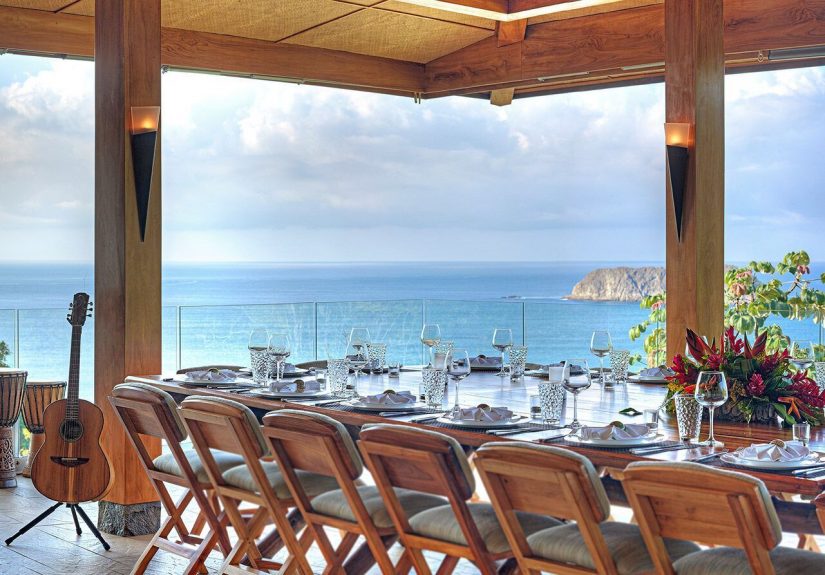 The dining area at Villa Panorama. Lots of chairs and a big table with the Pacific Ocean in the background