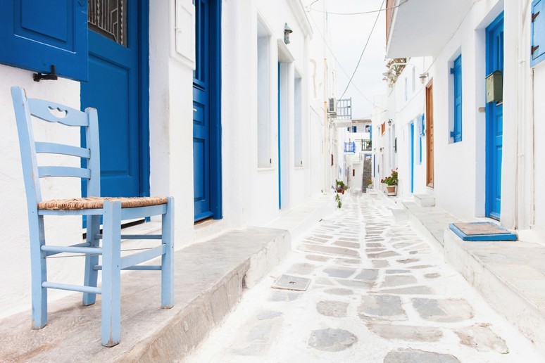 Bright white narrow street with vividly blue doors set into walls on a thin pavement