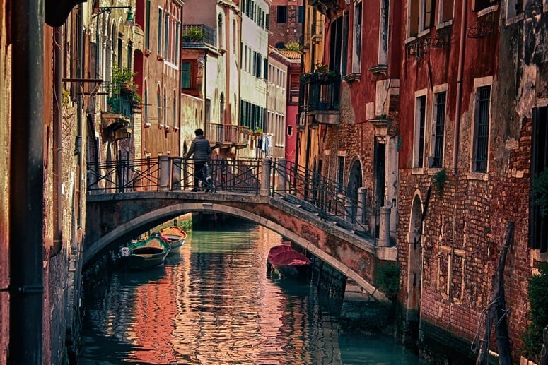 An old stone bridge spans the narrow canal between two rows of houses in Venice