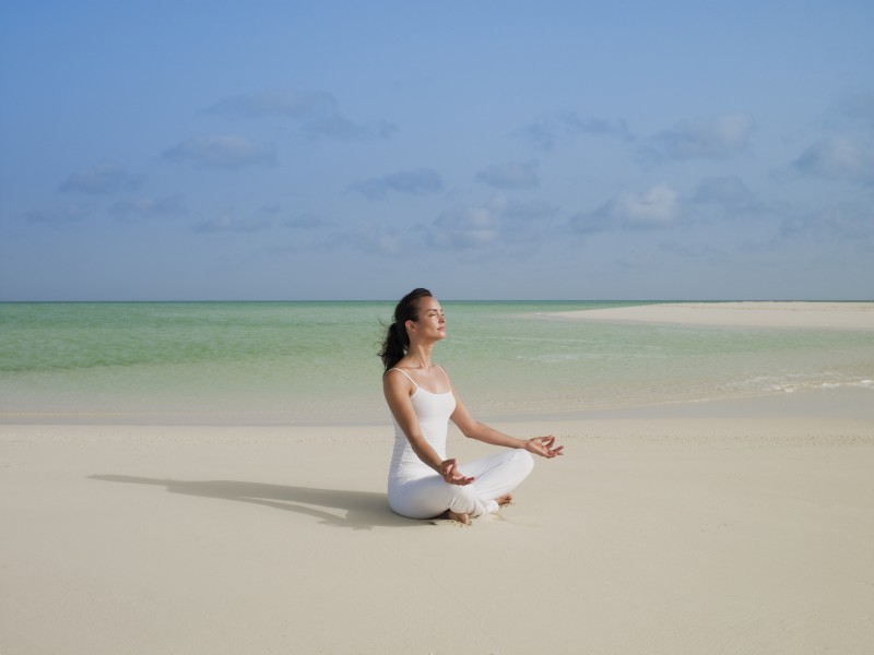 A girl in white meditates on the golden sandy beach at COMO Parrot Cay