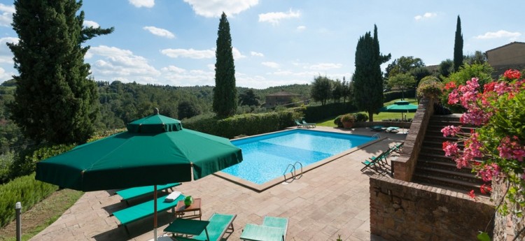 The pool, patio area, and gardens with distant pine forests and bright blue sky at Poggio Villa